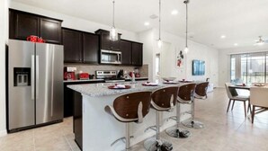 Una cocina moderna con armarios oscuros, electrodomésticos de acero inoxidable, una isla central con taburetes y luminarias colgantes.