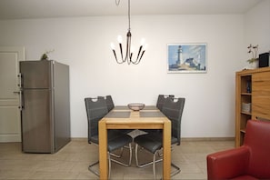 A compact kitchen with a refrigerator, a dining table with four chairs, a chandelier, and a painting on the wall. - Patio, free use of the AHOI adventure pool and sauna - Villa Antje FeWo 04 - (Göhren)