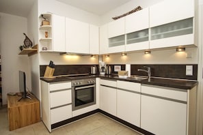 A modern kitchen with white cabinets, a black countertop, a built-in oven, and a coffee maker. - Patio, free use of the AHOI adventure pool and sauna - Villa Antje FeWo 04 - (Göhren)