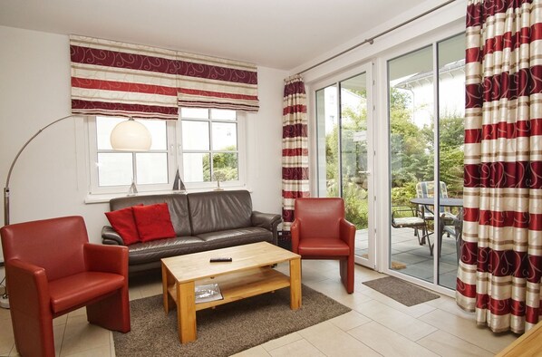 A living room with a sofa, two armchairs, a coffee table, and a large window with curtains.