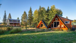 Dos cabañas con un patio cubierto de hierba y un bosque al fondo.