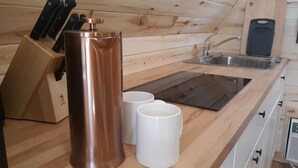 Una cocina con encimera de madera, un lavamanos, un bloque de cuchillos y dos tazas blancas.
