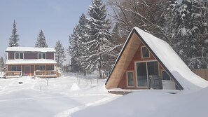 Une cabane dotée d’un toit en pente et d’une terrasse en bois, entourée d’arbres couverts de neige.