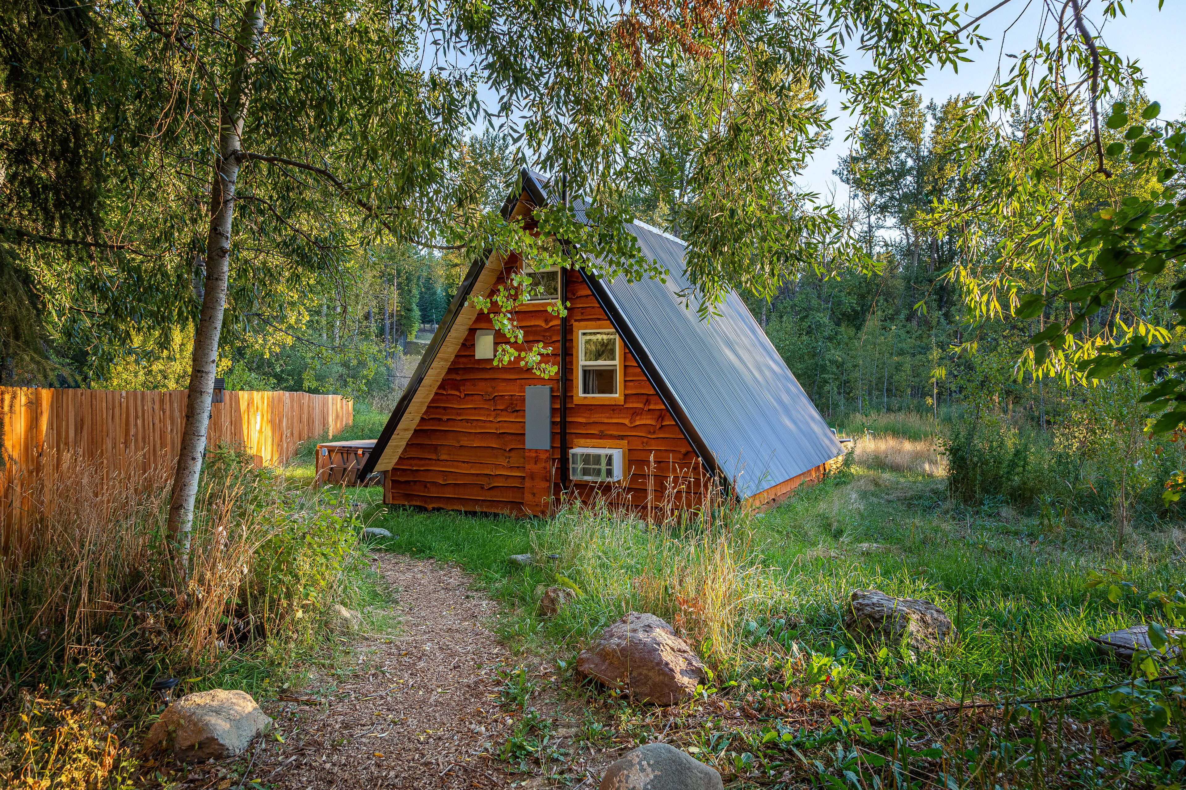 Une cabane en bois avec un toit en pente, entourée d’arbres et bordée d’un chemin de gravier.