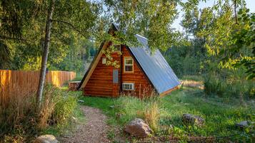 Une cabane en bois avec un toit en pente, entourée d’arbres et bordée d’un chemin de gravier.