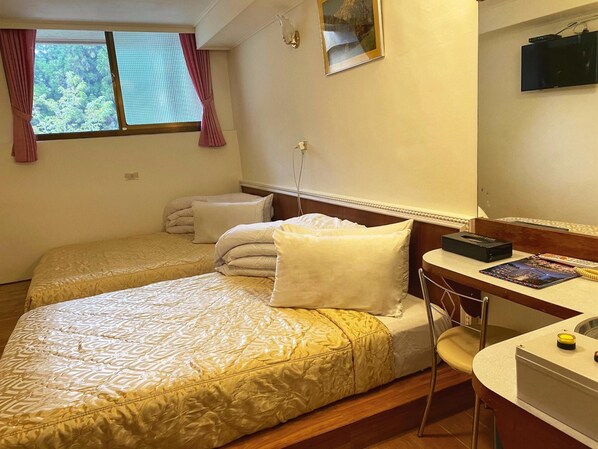 Camera d'albergo con due letti, una scrivania, una sedia, una TV e una finestra con tende.