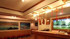 Een receptiegedeelte met een houten receptiebalie, ingelijste foto's aan de muur en een raam met uitzicht op bomen.