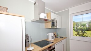 A compact kitchen with a built-in microwave, oven, and stovetop. It features a window with a view of a garden.