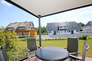A covered patio with a table and chairs, overlooking a residential area with houses and a grassy field.