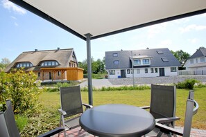 A covered patio with a table and chairs, overlooking a residential area with houses and a grassy field.