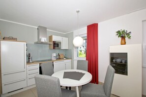 A compact kitchen with white cabinets, a microwave, and a coffee maker. There is a dining table with four chairs and a red curtain partially covering a window. - Beachfront vacation rental with a terrace, access to the pool and sauna - Rex Rugia H-1010 - (Göhren)
