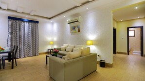 A modern living room with a sofa, dining table, and chairs. There is an air conditioning unit on the wall and a lamp on the side table.
