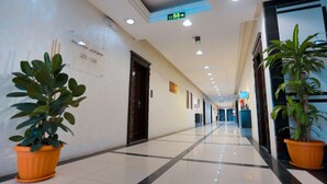 A hotel corridor with potted plants, a sign indicating room numbers, and a blue exit sign.