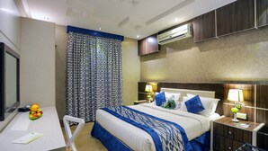 A hotel room with a bed, bedside table, lamp, air conditioning unit, and a desk with a chair.