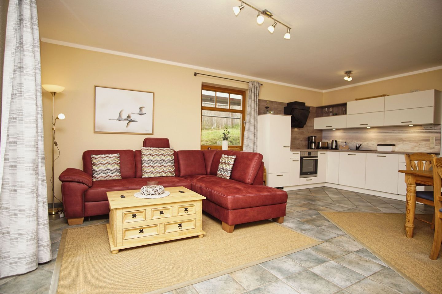 A living room with a red sofa, wooden coffee table, and a kitchen area with white cabinets and a stove.