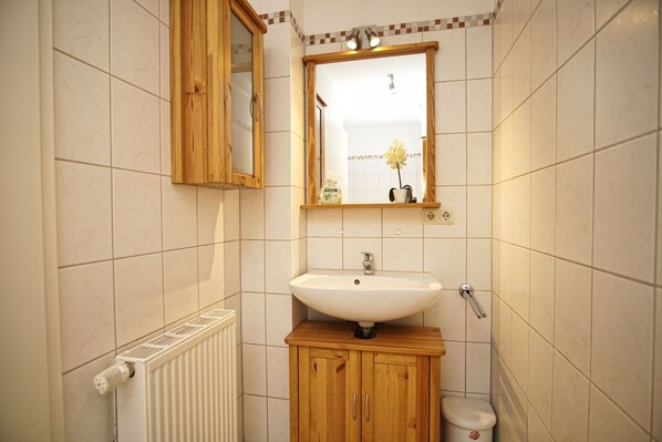Un baño pequeño con un armario de madera, un lavabo blanco, un espejo y un radiador.