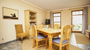 A dining area with a wooden table and chairs, a television, and a cabinet with shelves. - Haus Sonnenblume - idyllic location, vacation apartment with terrace, sea view - House (Putbus)