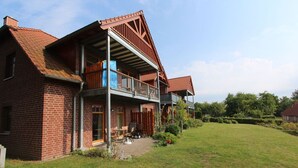 A two-story brick house with a balcony, a covered porch, and a well-maintained lawn. - Haus Sonnenblume - idyllic location, vacation apartment with terrace, sea view - House (Putbus)