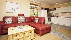 A living room with a red leather sofa, a wooden coffee table, and a kitchen area with white cabinets and a stove. - Haus Sonnenblume - idyllic location, vacation apartment with terrace, sea view - House (Putbus)
