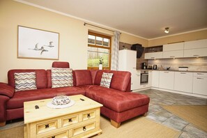 A living room with a red leather sofa, a wooden coffee table, and a kitchen area with white cabinets and a stove. - Haus Sonnenblume - idyllic location, vacation apartment with terrace, sea view - House (Putbus)
