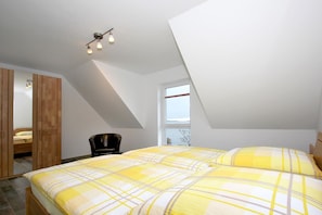 Un dormitorio con techo inclinado, una cama con ropa de cama amarilla y blanca, un armario de madera, una silla y una ventana con vistas.
