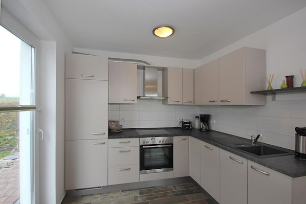 Una cocina moderna con armarios blancos, horno empotrado, cafetera y ventana con vistas al exterior.