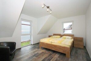 Une chambre avec un plafond en pente, un lit avec une literie jaune, une table de chevet en bois, une chaise et une fenêtre donnant sur l’extérieur.