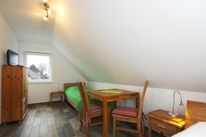 Ein kleines, helles Schlafzimmer im Dachgeschoss mit einem Bett, einem Holztisch, einem Stuhl und einem Fernseher auf einem Schrank.