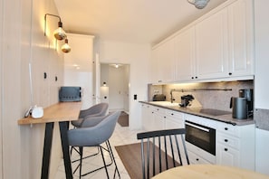 A modern kitchen with white cabinets, a wooden countertop, a coffee machine, and a microwave. There is a small dining area with a table and two chairs.