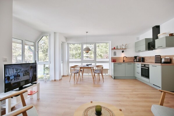 A modern kitchen with a dining area, large windows, and a flat-screen TV.