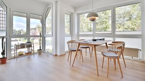 A spacious room with large windows, a dining table with chairs, and a hanging light fixture. - Gorch-Fock-Str 16 Apartment 6 - Gorch-Fock-Str 16 (Timmendorfer Strand)