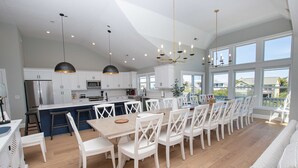 A spacious kitchen with white cabinetry, a central island, and a dining area with white chairs. - Oceanside, 8 BRs, Private Pool, Theater Room, Rec Rm, Hot Tub, OL126, Knot Tide Up (Corolla)