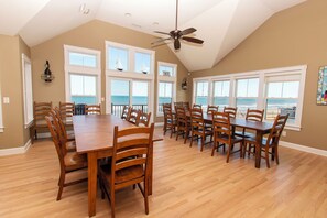 A dining area with a large wooden table and chairs, large windows with ocean views, and a ceiling fan. - OCEANFRONT, 10 BRS, ELEV, Pool, Rec Rm, Theater Rm, OH1251, Beach Plaza (Corolla)