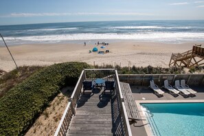 A wooden deck with a pool, lounge chairs, and a table overlooking a beach. - OCEANFRONT, 10 BRS, ELEV, Pool, Rec Rm, Theater Rm, OH1251, Beach Plaza (Corolla)