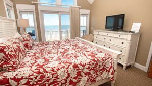 A bedroom with a large bed, a television on a dresser, and a view of the ocean through the windows. - OCEANFRONT, 10 BRS, ELEV, Pool, Rec Rm, Theater Rm, OH1251, Beach Plaza (Corolla)