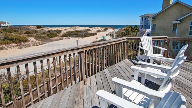 A wooden deck with white Adirondack chairs overlooking a sandy beach and ocean. - Semi-Oceanfront, Close to Beach Access, Private Pool, Hot Tub, 109, Happy Ours (Corolla)