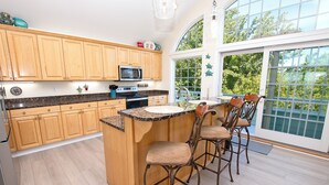 A kitchen with wooden cabinets, a granite countertop, a built-in microwave, and a dining area with bar stools. - Soundfront, ELEV, Private Pool, Pool Table, Water Views, VOH1, Soundly Sea-Cluded (Corolla)