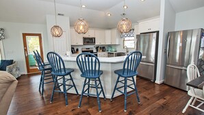 A modern kitchen with white cabinets, stainless steel appliances, and blue bar stools.
