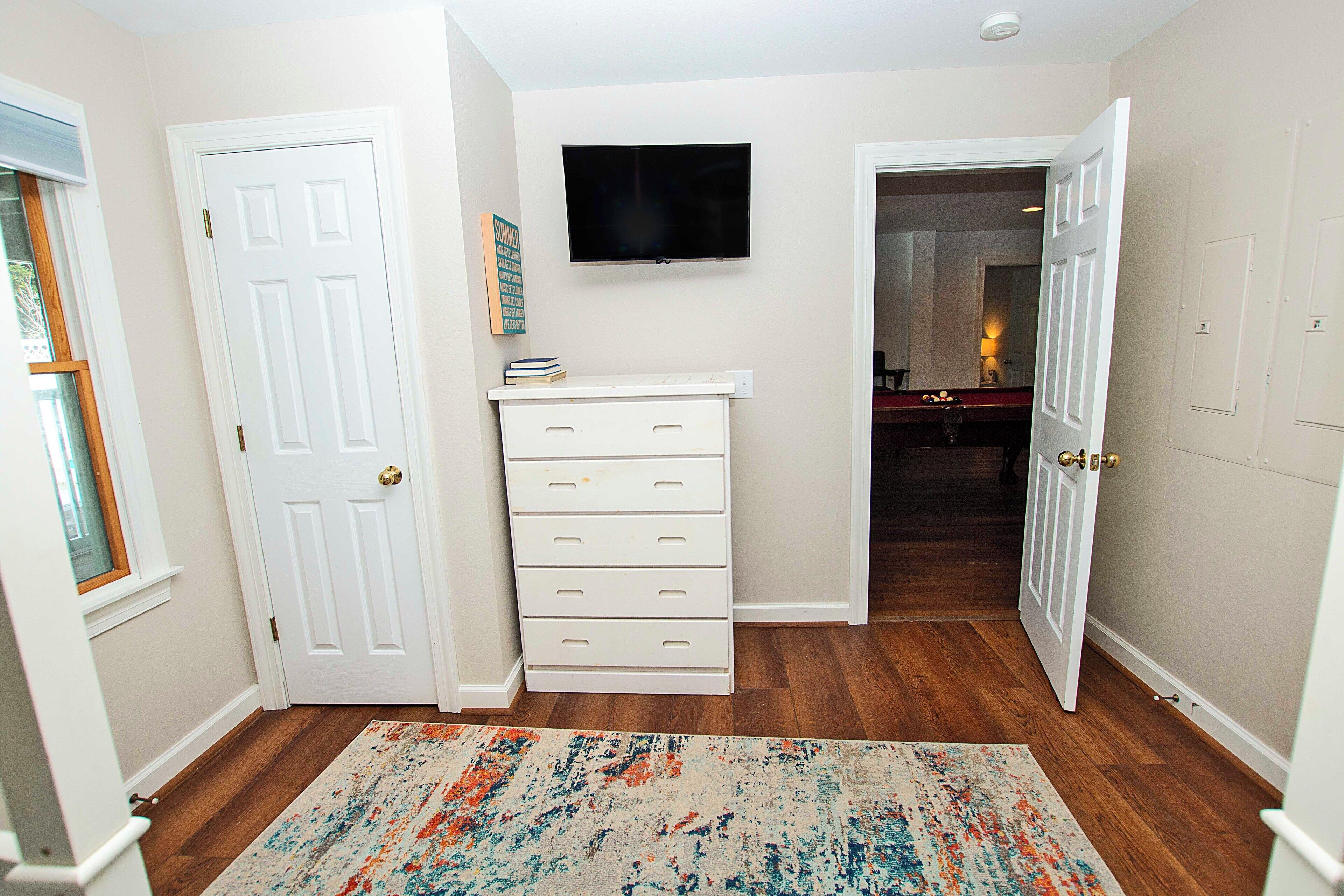 A hallway with a white door, a white dresser, and a television mounted on the wall.