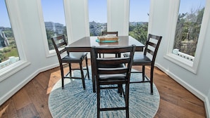 A dining area with a table and four chairs, large windows, and a view of houses and trees.