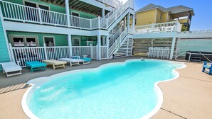 A swimming pool with a white deck, surrounded by white railings and blue lounge chairs.