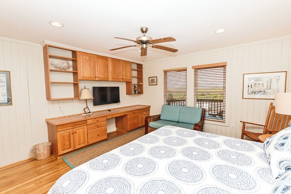 A bedroom with a bed, wooden furniture, a ceiling fan, and a TV.