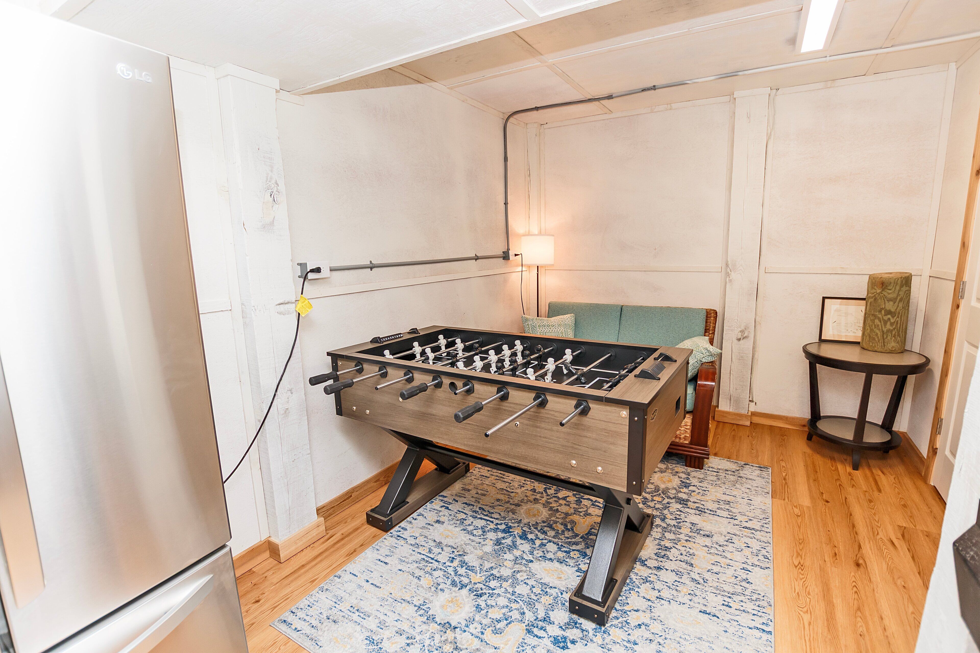 Ein Raum mit einem Kicker, einer Couch, einem kleinen runden Tisch und einer Lampe.