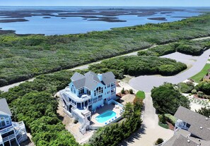 A large house with a swimming pool, surrounded by lush greenery and a view of the ocean.
