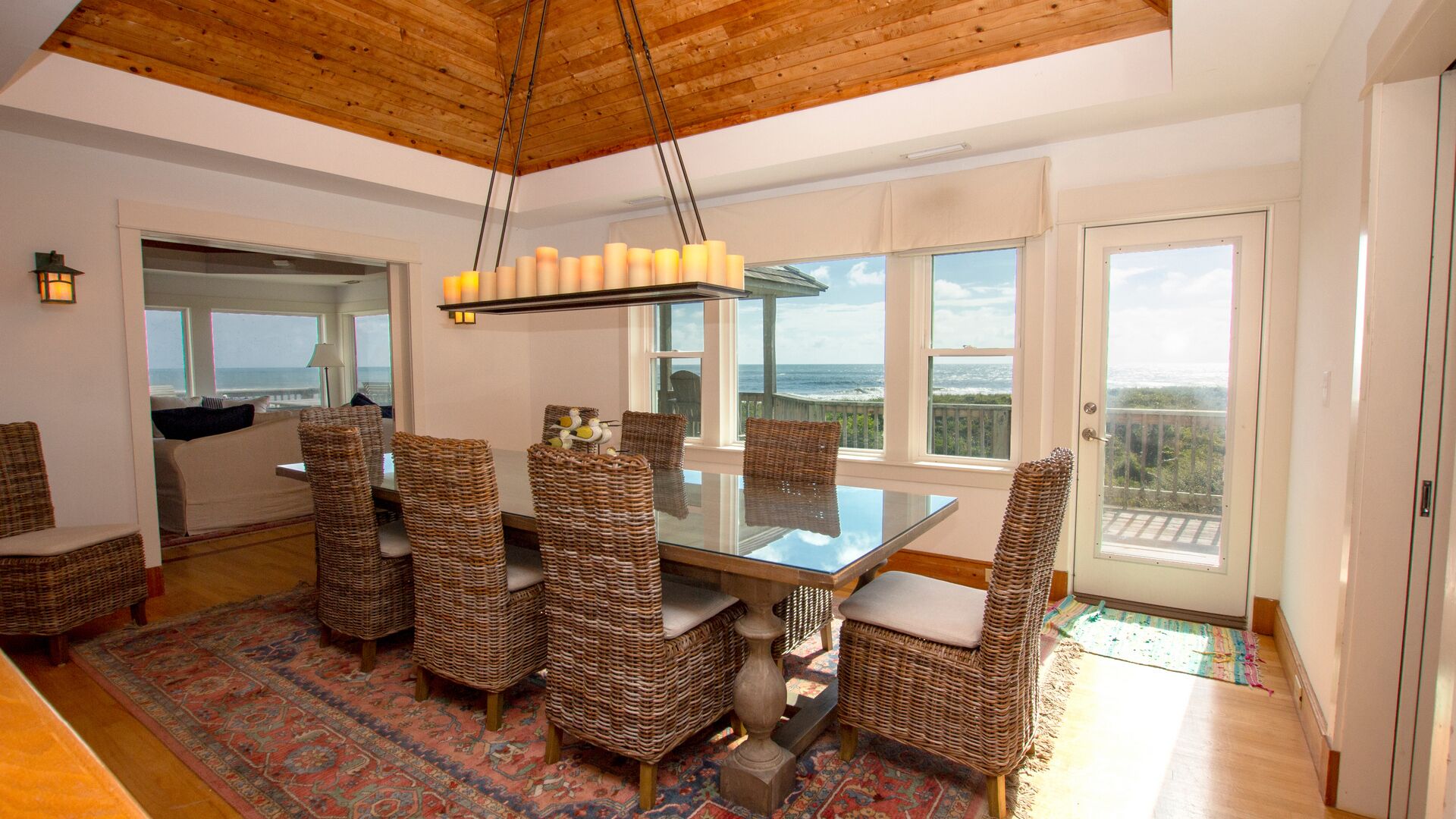 A dining area with a glass table and wicker chairs, overlooking a scenic ocean view.
