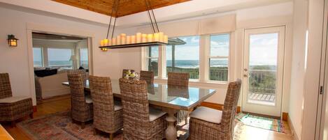 A dining area with a glass table and wicker chairs, overlooking a scenic ocean view.