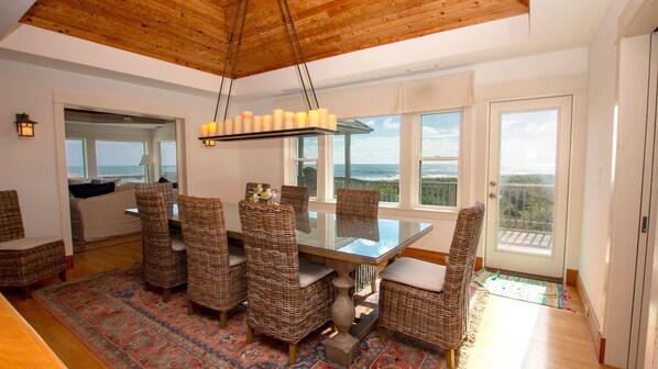 A dining area with a glass table and wicker chairs, overlooking a scenic ocean view.