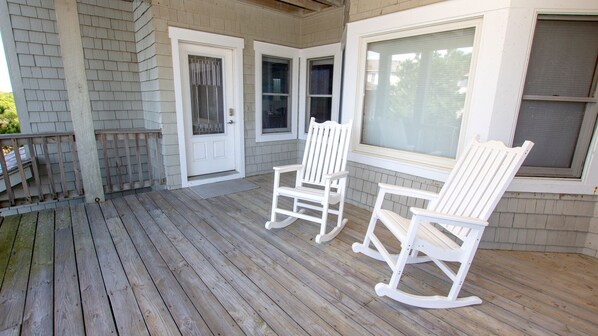 A porch with two rocking chairs, a wooden deck, and a white door with a window.