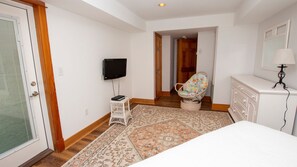 Ein Schlafzimmer mit einem Bett, einem Fernseher, einem Korbstuhl, einer Kommode und einem gemusterten Teppich.