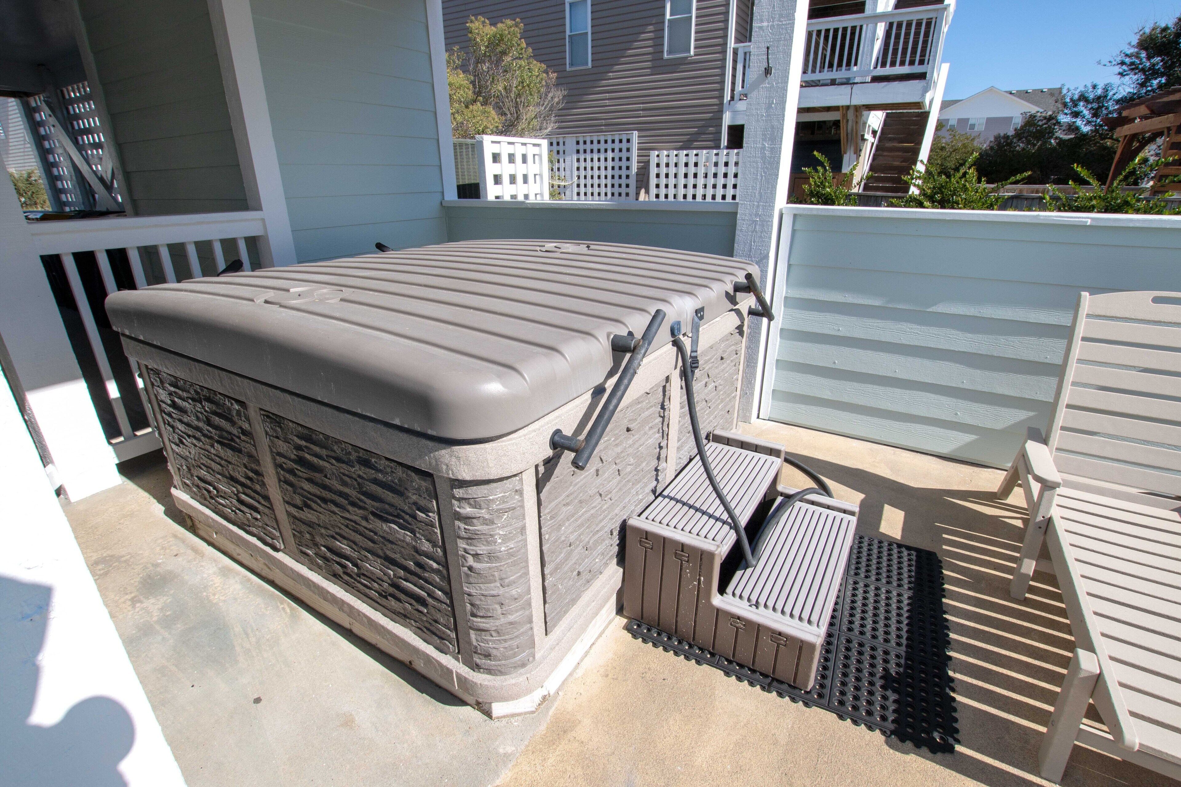 A hot tub with a built-in seat and steps, located in a covered outdoor area with a concrete floor.
